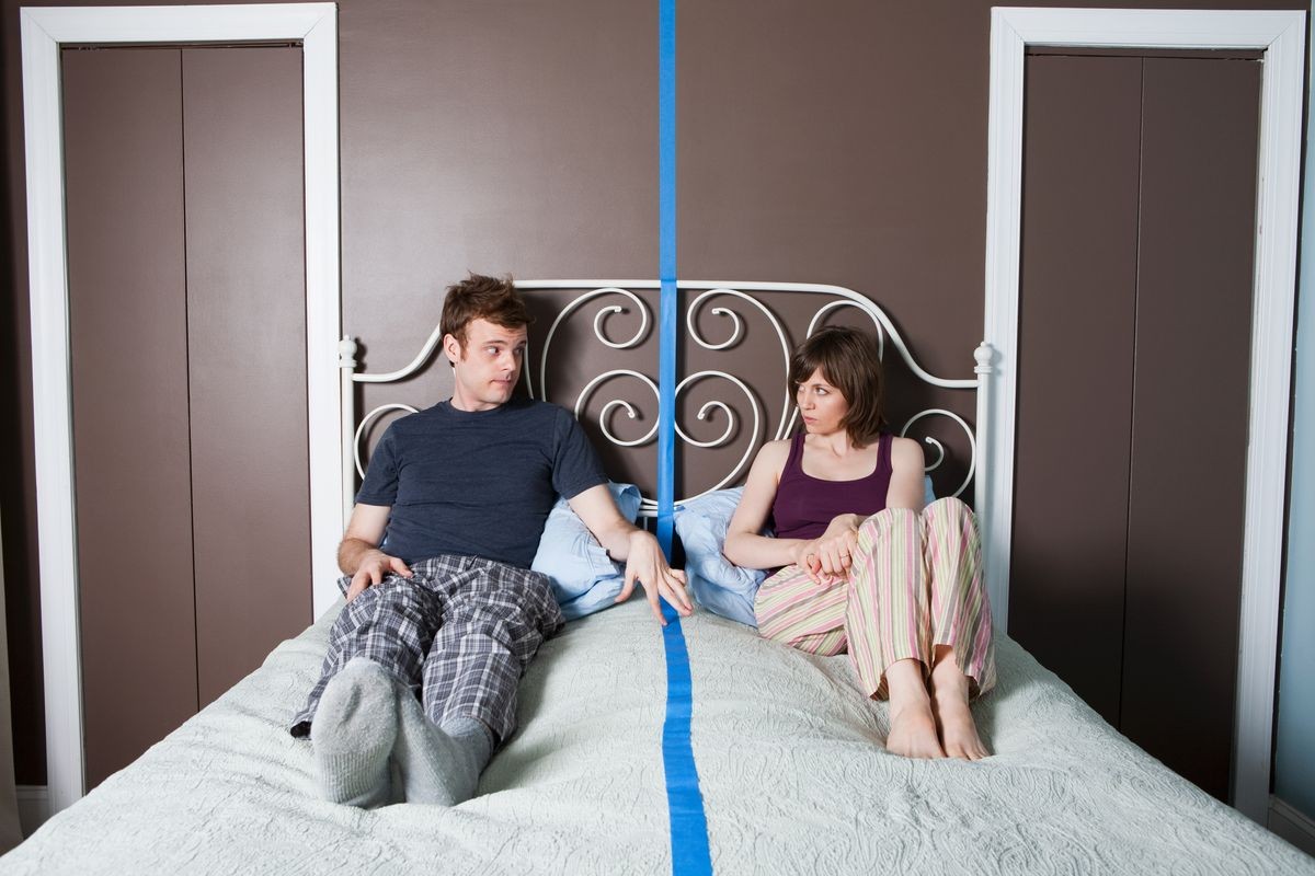 Young couple sitting on bed separated by blue line