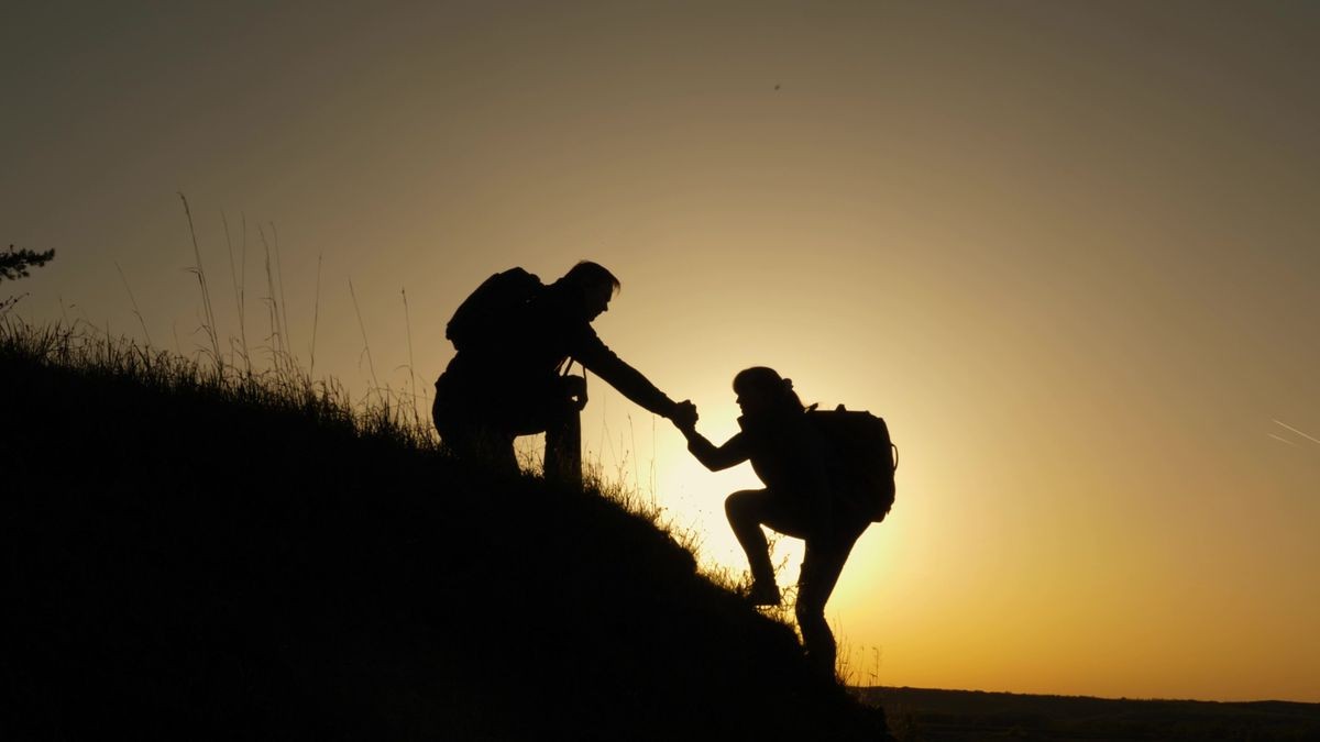 traveler man extends his hand to a girl climbing to the top of hill. travelers climb the cliff holding hand. teamwork of business people. Happy family on vacation. tourists hug on top of mountain